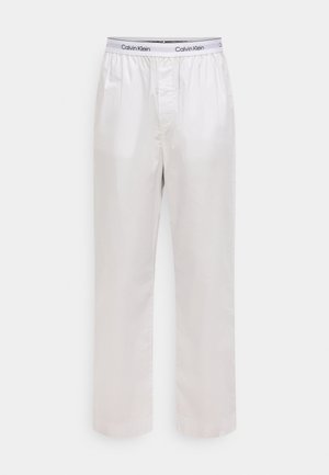 Pantalones de algodón blancos para estar en casa con cintura elástica que lleva una banda negra con logo. Diseño de pierna recta y textura suave y ligera.