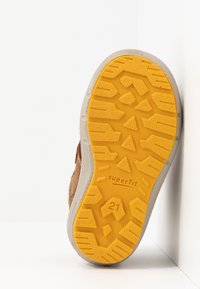 Zapato de ante marrón con una suela de goma amarilla texturizada, que presenta un patrón de agarre y la marca "superfit", con la talla 21 embostada en la suela.