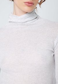 Světlá šedá roláková svetr vyrobený z měkkého a pružného materiálu. Přiléhavý střih s vysokým límcem a jemnou strukturou po celém povrchu.