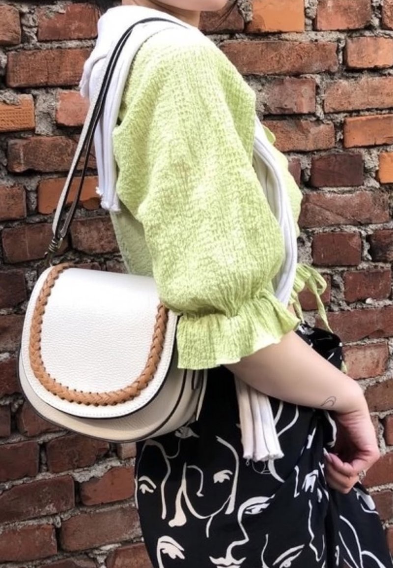 Witte leren zadelhandtas met gevlochten bruine accenten, crossbody gedragen. Model in een lichtgroene textuurblouse en een zwart met patroonrok.