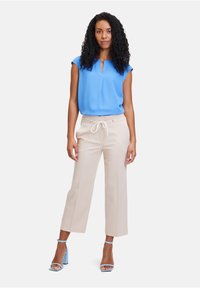 Blauwe blouse met korte mouwen en een ronde halslijn, gecombineerd met beige high-waisted wijde broek en lichtblauwe haksandalen.
