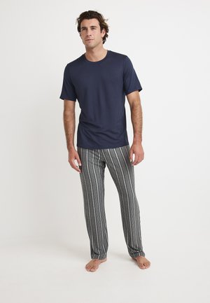 Marineblauwe t-shirt met korte mouwen gecombineerd met grijs-witte gestreepte pyjamabroek. Zachte stof, relaxte pasvorm, staand op blote voeten tegen een lichte achtergrond.