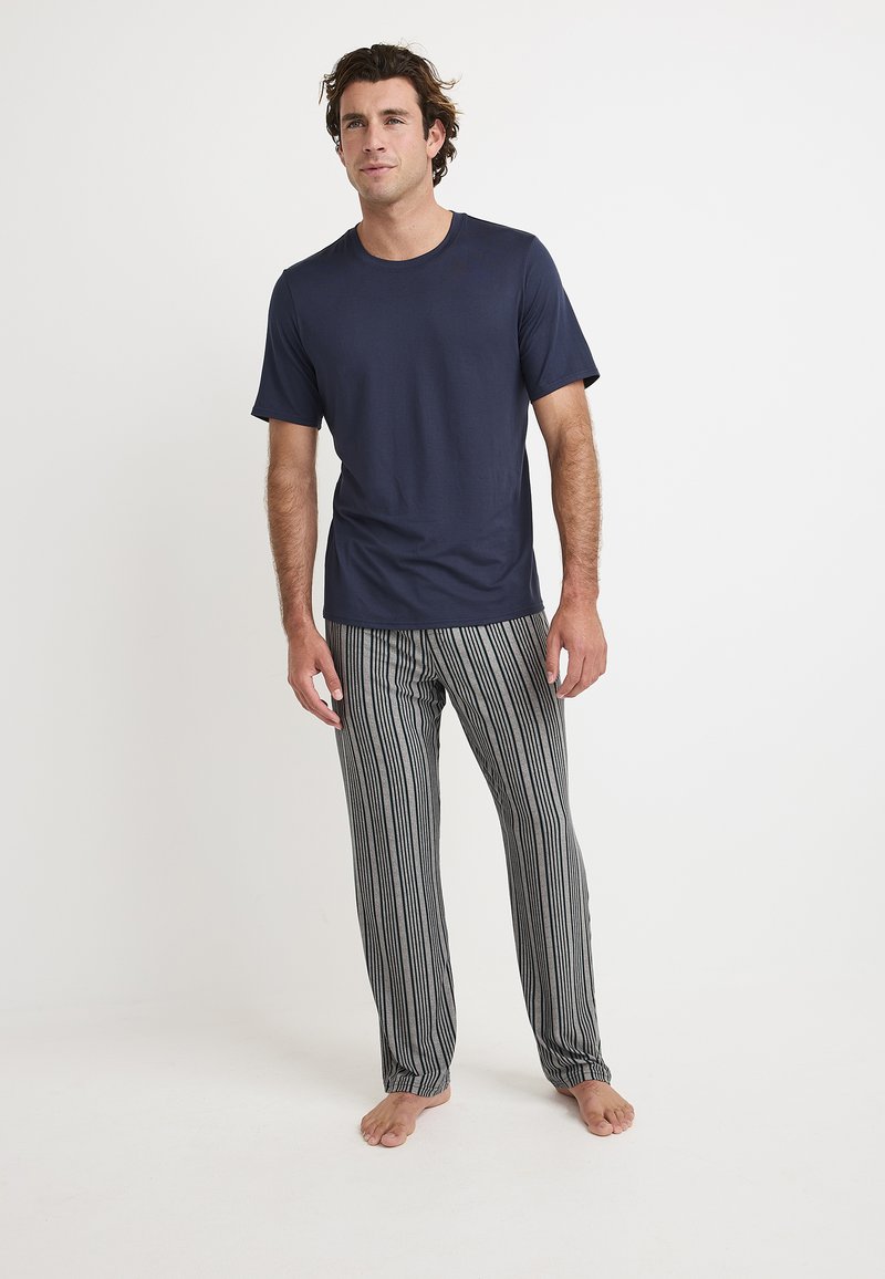 Marineblauwe t-shirt met korte mouwen gecombineerd met grijs-witte gestreepte pyjamabroek. Zachte stof, relaxte pasvorm, staand op blote voeten tegen een lichte achtergrond.