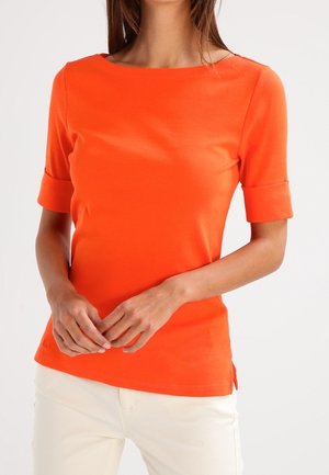 Pomarańczowa bluzka z krótkim rękawem i okrągłym dekoltem. Posiada podwinięte mankiety i boczne rozcięcia. Wykonana z miękkiego, gładkiego materiału. Noszona z jasnymi spodniami.