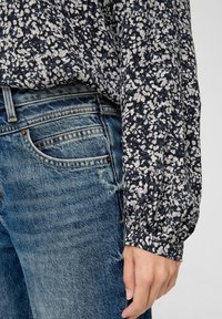 Marinebluse mit blumigem Muster in Weiß, langen Ärmeln und elastischen Bündchen, kombiniert mit lässigen, blauen Jeans im klassischen Schnitt.