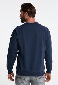 Granatowy sweatshirt z okrągłym dekoltem, z ribbowanymi mankietami i detalem szwowym na plecach. Zawiera małe logo na lewej rękawie.