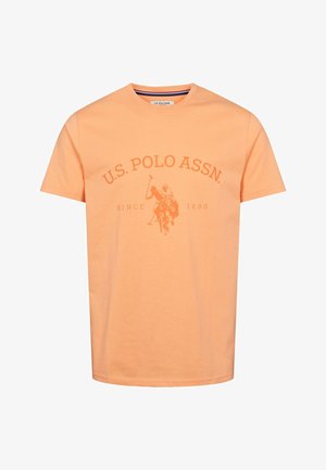 Pomarańczowa bawełniana koszulka z okrągłym dekoltem, z centralnym nadrukiem przedstawiającym gracza polo oraz napisem "U.S. POLO ASSN." poniżej. Krótkie rękawy, standardowy krój.