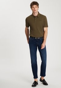 Oliwkowa koszulka polo z kołnierzykiem, zestawiona z ciemnoniebieskimi dżinsami. Czarny pasek z srebrną klamrą i czarne mokasyny dopełniają strój.