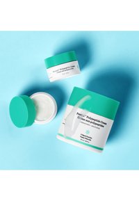 Two skincare cream jars with teal lids. One larger (50 ml) and one smaller (15 ml) with white labels featuring text and a pattern. Cream inside visible.