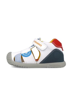 Sandal bianco con design a punta chiusa e ritagli, suola in gomma grigia e accenti colorati in blu, rosso e giallo. Cinturino regolabile.