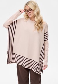 Beige oversized trui met bruine horizontale strepen. Zachte gebreide textuur, ronde halslijn en zijsplitten voor bewegingsvrijheid.