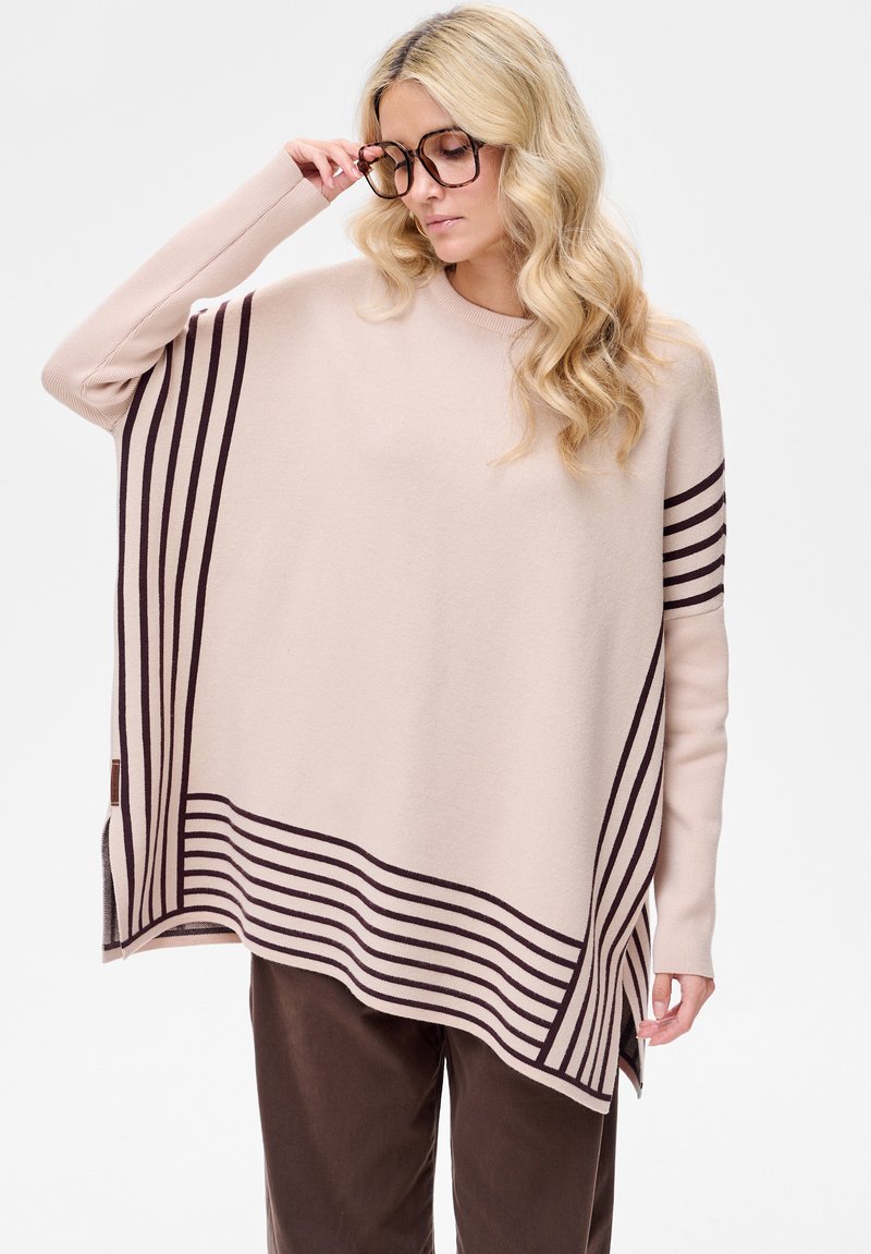 Beige oversized trui met bruine horizontale strepen. Zachte gebreide textuur, ronde halslijn en zijsplitten voor bewegingsvrijheid.