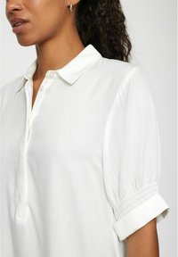 Weiße Bluse mit kurzen Ärmeln und geknöpftem Kragen, mit glatter Textur und Raffung an den Ärmeln.