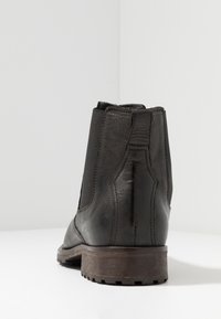 Bottine en cuir noir avec panneaux latéraux élastiques, bout arrondi et talon en bois brun texturé. Finition lisse et construction solide.