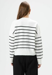 Witte trui met zwarte horizontale strepen, geribde zoom en losse pasvorm. Heeft verlengde schouders en zachte, gestructureerde stof.