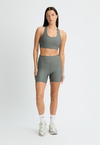 Un reggiseno sportivo grigio e degli shorts a vita alta abbinati, realizzati in un tessuto testurizzato e elastico. Indossati con calze bianche e scarpe da ginnastica di colore chiaro.
