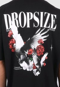 Black t-shirt featuring a graphic print of white doves and red flowers, with bold text "DROPSIZE" and "EST 2020" in white. Cotton material.
