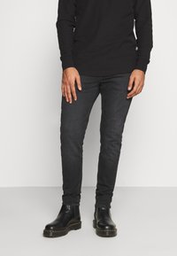 Camisa negra de manga larga combinada con jeans de denim oscuros, con un corte ajustado. Botas de cuero negras con suela gruesa completan el conjunto.