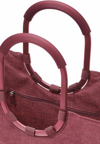 Rote strukturierte Stofftasche mit zwei geschwungenen Griffen, gerippter Griffoberfläche und einer Außenreißverschlusstasche für sicheren Stauraum.