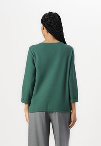 Grön, texturerad topp med trekvartsärmar och rund halsringning, i kombination med ljusgrå, skräddarsydda byxor. Enkelt och avslappnat design.