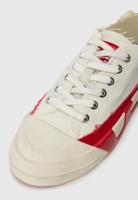 Baskets en toile avec un dessus blanc, des accents rouges et une semelle en caoutchouc texturé. Comprend des lacets blancs et des détails de couture visibles.