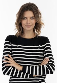 Fekete-fehér csíkos pulóver, kerek nyakkal, hosszú ujjak és bordázott mandzsetták, egy karját keresztbe tett személyen.