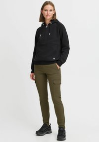 Felpa nera con cappuccio e tasca frontale a marsupio, abbinata a pantaloni cargo color oliva con tasche laterali e scarpe da ginnastica nere.