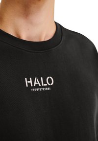 Czarna bluza z okrągłym dekoltem, z białym nadrukiem "HALO 1968 1972 1981" na piersi, o miękkim, teksturowanym wykończeniu.