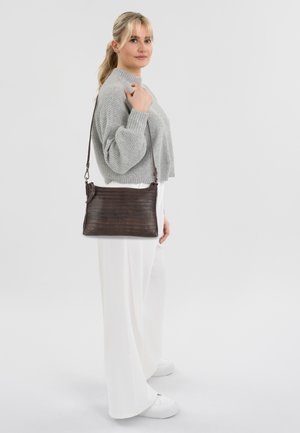 Borsa a spalla texture marrone con una forma elegante, dotata di una tracolla lunga. Indossata con un maglione grigio e pantaloni larghi bianchi.