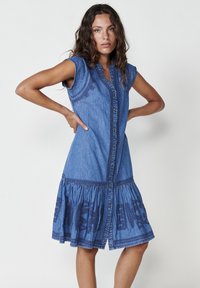 Abito di denim con bottoni frontali, maniche corte e gonna svasata. Presenta ricami blu all'orlo e dettagli di cucitura testurizzati.