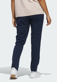 Marinblå sportbyxor med smal passform, tillverkade av lätt tyg, med fickor och matchade med vita sneakers.