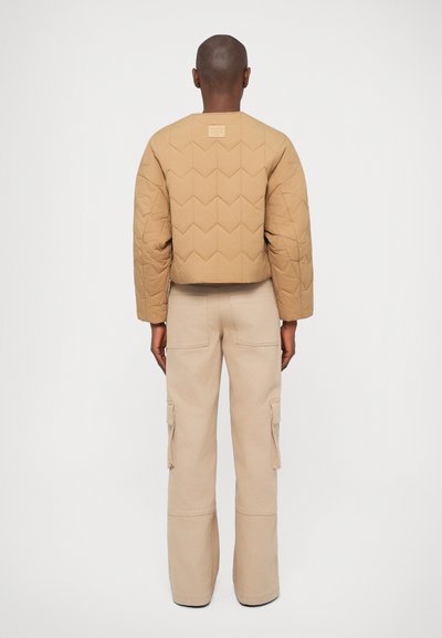 Giacca trapuntata marrone con una vestibilità corta, caratterizzata da un motivo a V. Abbinata a pantaloni cargo beige con tasche laterali e una forma morbida.