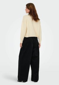 Lichtbeige cropped sweater met ribgebreide boorden, gecombineerd met losse zwarte corduroy broek met een hoge taille en wijde pijpen.