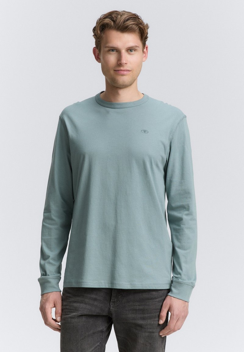 Langarmshirt aus weichem Baumwollstoff in einem hellen Türkis, mit Rundhalsausschnitt und kleinem Logo auf der Brust.
