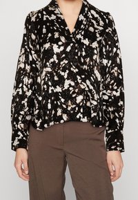 Blusa astratta in bianco e nero con motivo, maniche lunghe, scollo a V senza colletto e vestibilità rilassata, realizzata in un tessuto strutturato.