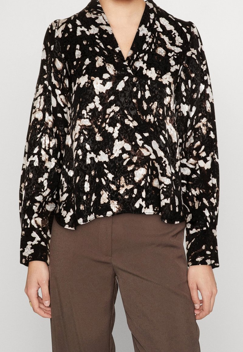 Blusa astratta in bianco e nero con motivo, maniche lunghe, scollo a V senza colletto e vestibilità rilassata, realizzata in un tessuto strutturato.