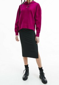 Magenta huvtröja med snörning och ribbade ärmslut, i kombination med en svart ribbad pennkjol med sidoklyvning, bärs med svarta snörskor.