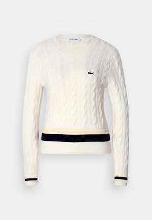 Krem pulover v kabelskem pletenju s krojnim ovratnikom, ki ima črtasto mornarsko modro in rumeno obrobo. Logo Lacoste je izvezen na levem prsnem delu.