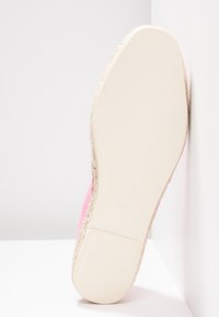Semelle d'une espadrille rose avec semelle en caoutchouc blanche et bord en jute tissé, taille 39, reposant verticalement contre un mur blanc.