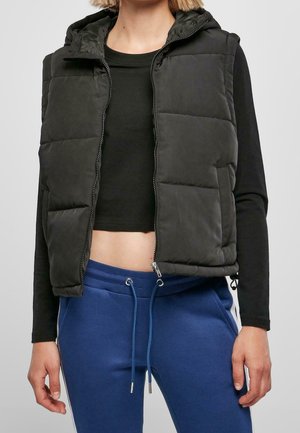 Personne portant un haut noir court à manches longues, un gilet matelassé noir et un pantalon de survêtement bleu avec cordons.