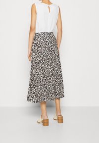 Falda con estampado de leopardo y diseño fluido, hecha de tela ligera, combinada con una blusa blanca sin mangas que presenta un detalle de abertura en la espalda.