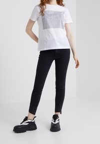 White cotton t-shirt with vertical black striped graphic reading "DRY WORK." Paired with black skinny jeans featuring studded hem and chunky black sneakers.