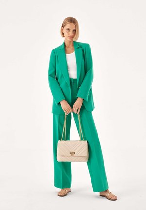 Zelený tailored blazer a odpovídající kalhoty, spojené s bílým topem a béžovou prošívanou kabelkou se zlatými řetízky. Hladká tkanina, slim fit.