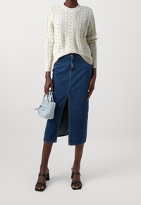 Cream knit sweater with a textured pattern, high-waisted denim pencil skirt with front slit, black block-heeled sandals, and light blue handbag.