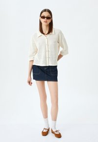 Lettrør, cremede farvet strikknappet skjorte med krave, parret med en mørk denim mini skirt. Brune ruskind mokkasiner og hvide sokker.