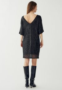 Rochie neagră cu paiete, cu decolteu în V, mâneci scurte și lungime până la genunchi. Prezintă o croială lejeră și un strat din material transparent la tiv.