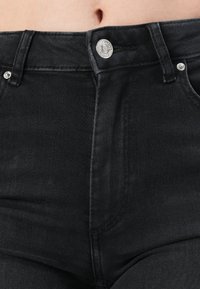 Hoge taille zwarte jeans van denim, met een zilveren knoopsluiting, twee voorknoopzakken en een gestructureerde stof.