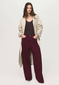 Beige trenčkot přes tmavý top, spárovaný s vínovými širokými kalhotami. Mezi vlastnosti patří volný střih a detaily kapes.