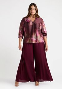 Blusa multicolore con una texture liscia, scollatura a V profonda, maniche a tre quarti, abbinata a pantaloni larghi plissettati bordeaux e sandali leggeri.