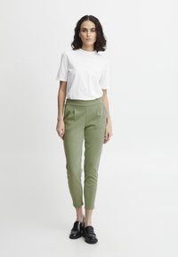 Witte t-shirt met korte mouwen, gecombineerd met lichtgroene, op maat gemaakte broek met plooien, slim fit en zwarte instappers. Eenvoudig ontwerp en effen kleuren.